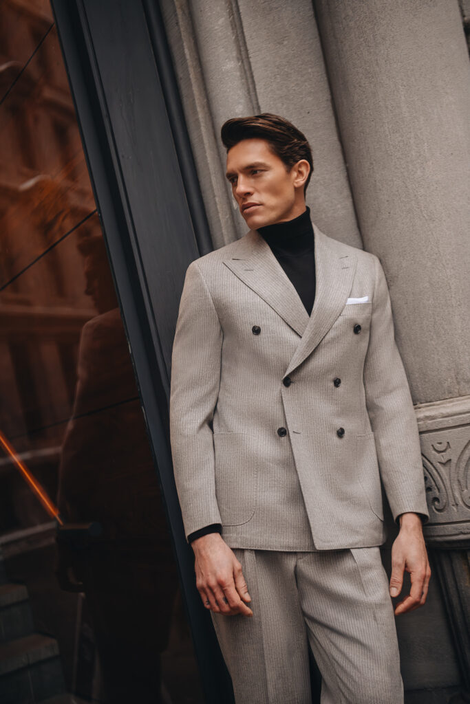 Model wearing a light grey double-breasted suit with a black turtleneck